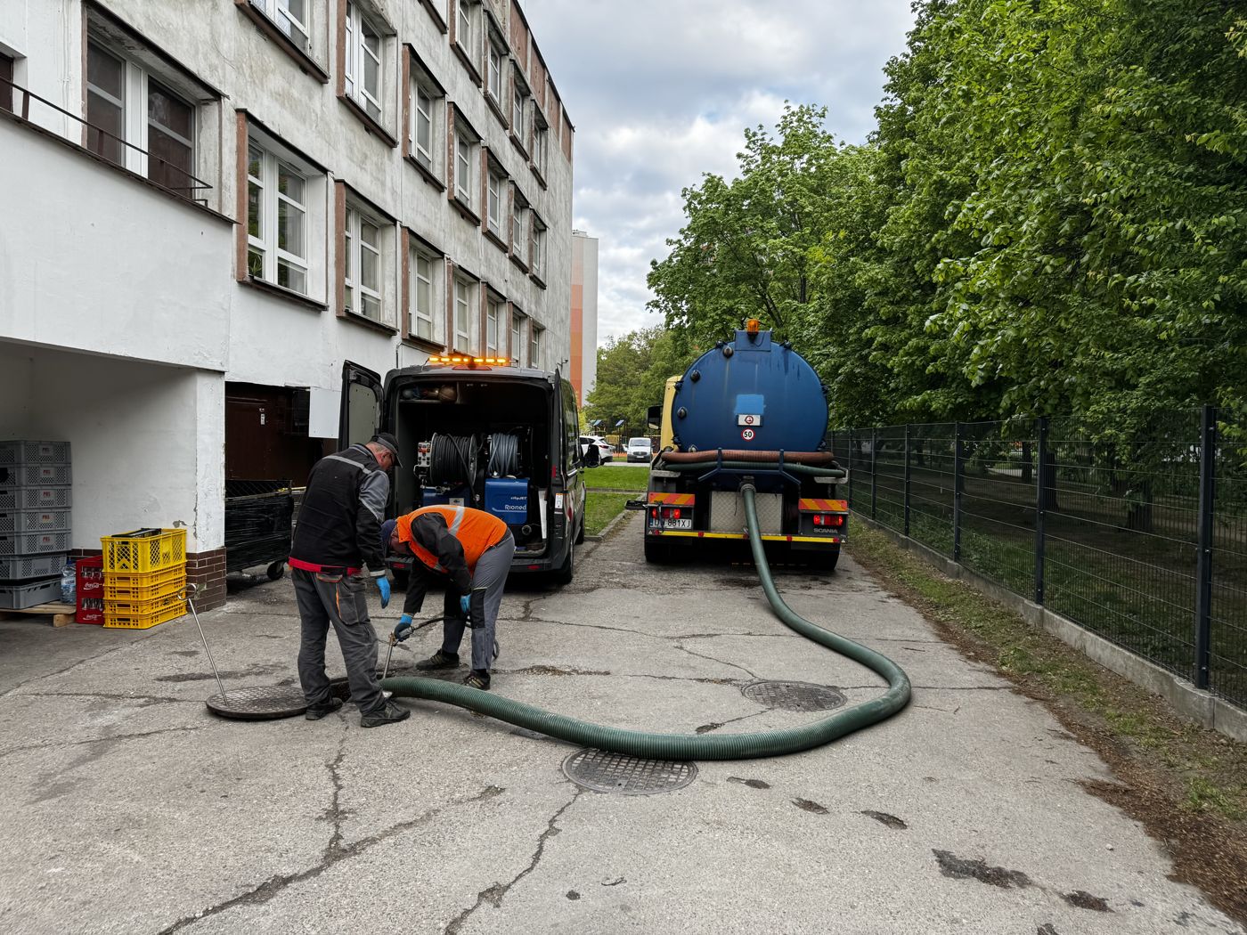 Brygada ZIĘBUD EXPERT przy otwartej studzience na osiedlu; obok bus serwisowy i wóz asenizacyjny WUKO z rozłożonym wężem ssawnym