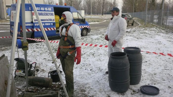 Zimowa praca przy studni kanalizacyjnej: trójnóg z wciągnikiem, pracownik w kombinezonie ochronnym i maceberek oraz oznakowany bus z napisem awarie24h.pl