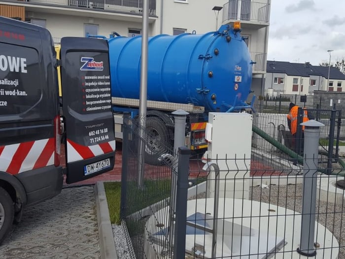 Pojazdy serwisowe ZIĘBUD — bus wodociągowy i wóz asenizacyjny przy przepompowni na osiedlu we Wrocławiu